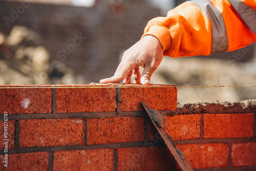 Canvas Print Bricklayer laying another brick in the wall on construction site for sturdy wall