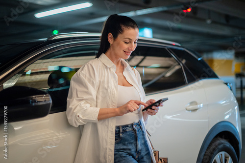 Brunette haired woman standing next to her car in parking garage and using smart phone