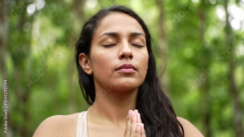 Young woman calmly meditating while doing yoga breathing exercises with eyes closed and feeling peace of mind