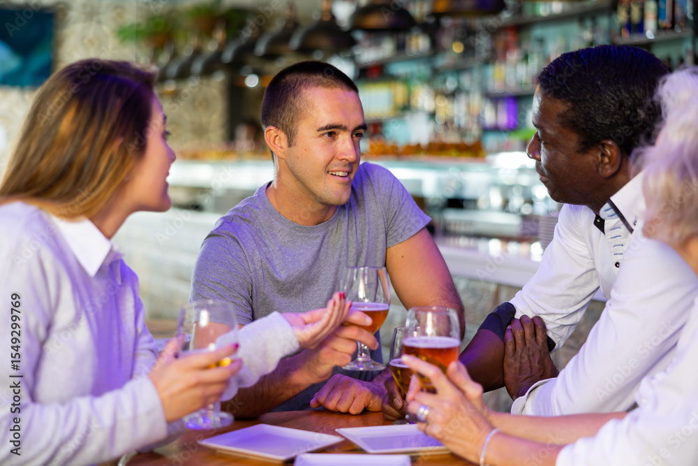 Fototapeta premium Spending time in bar. Four positive friends drinking beer in bar