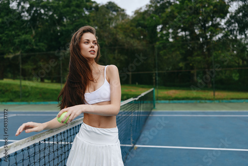 Young athletic woman in sporty outfit playing tennis on an outdoor court surrounded by lush greenery, showcasing confidence and enjoyment in her sport