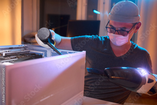 A man cleans a computer case with a vacuum in a bright room, stressing workspace tidiness