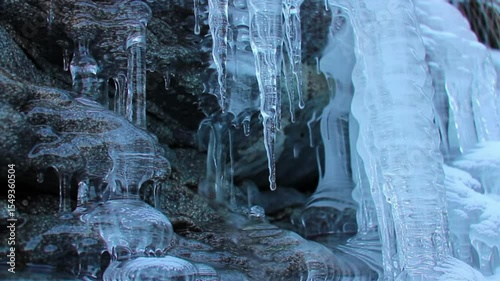 Close-up of natural ice formations and icicles hanging from a cold, rocky surface in a winter landscape or mountain area