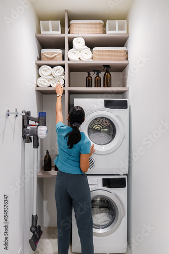 Woman organizing towels in modern laundry room with washing machine and storage shelves