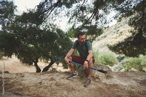 Male Hiker Resting with Trekking Pole Surrounded by Scenic Forest