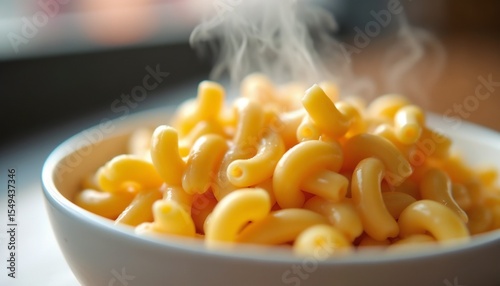 A bowl of steaming macaroni pasta. The pasta is yellow and shaped in curved tubes. The background is softly blurred, emphasizing the dish.
