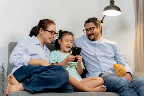 Asian parents and their 8-year-old daughter enjoying time together while using smartphones at home.