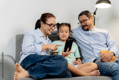 Asian parents and their 8-year-old daughter enjoying time together while using smartphones at home.