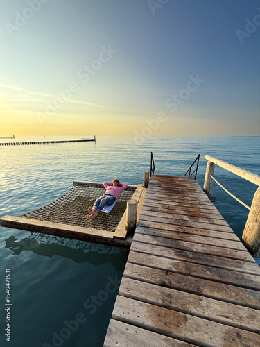 relaxing woman on a water net hammock over the water in sunset light