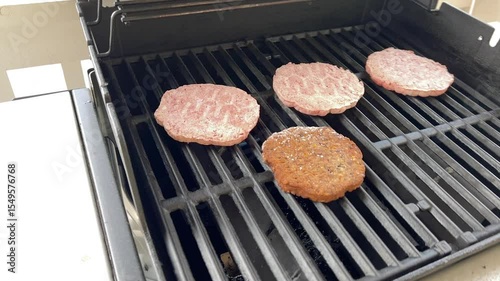 Raw hamburger patties cooking on open gas grill