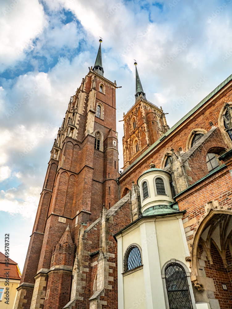 Fototapeta premium Beautiful view of a Gothic brick Collegiate Church of the Holy Cross, St Bartholomew featuring twin towers and detailed architecture, surrounded by a bright cloudy sky, Wroclaw, Poland