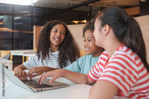 Smiling Three Diverse little girls learning together on a laptop in a classroom, showing joy, Multiethnic children with E-learning and online classroom in a relaxed educational.