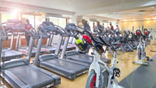 Blurred background modern gym filled with treadmills and exercise bikes. Bright lighting and morning sun highlight a clean and active fitness environment, promoting health and cardio training.