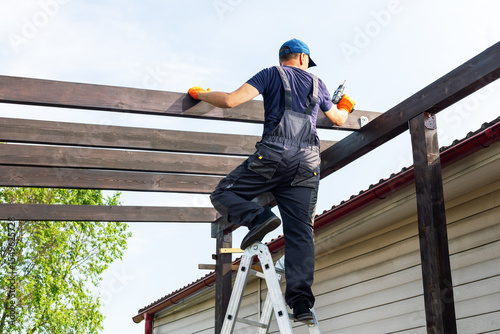  builder man with electric screwdriver installing impregnated wooden board. man  builds a wooden terrace near his house.
