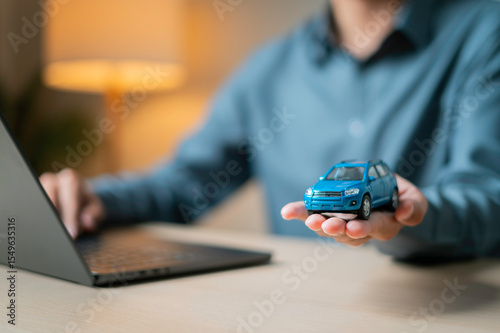 Signing auto insurance contract with car key and model car with a laptop in the foreground representing digital auto loan and buying process.