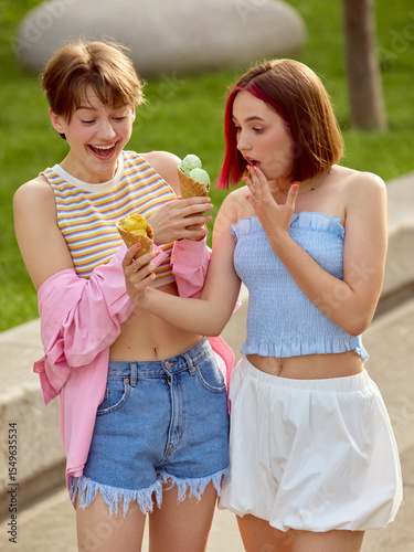 Two friends, gen z, enjoy ice cream treats on a sunny day in a vibrant park. Concept of friendship and joyful outdoor moments.