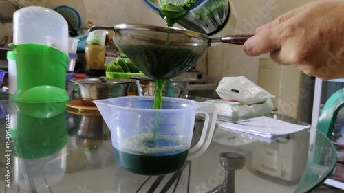 Scene Preparing homemade green juice using a strainer and kitchen utensils in a cozy home environment.
