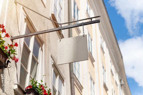 Hanging square shop sign with floral decor and sunny sky, ideal for boutique branding mockups, cafes or local small business advertisements