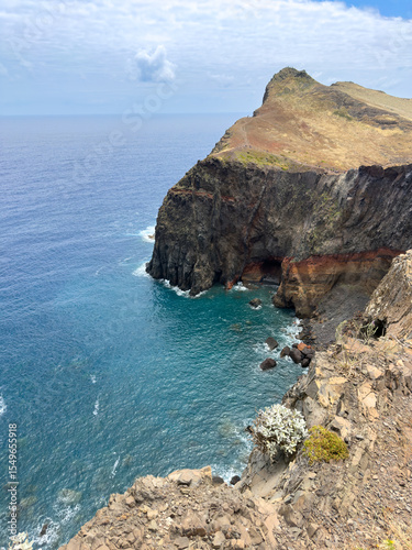 High cliffs on the shore of a small bay on the island of Madeira with a high rocky coastline, huge stones and ocean waves.