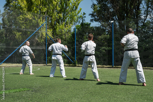 Group of men practicing karate outdoors on sunny day.
