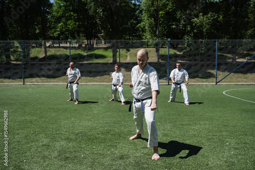 Group of men practicing karate outdoors on sunny day.