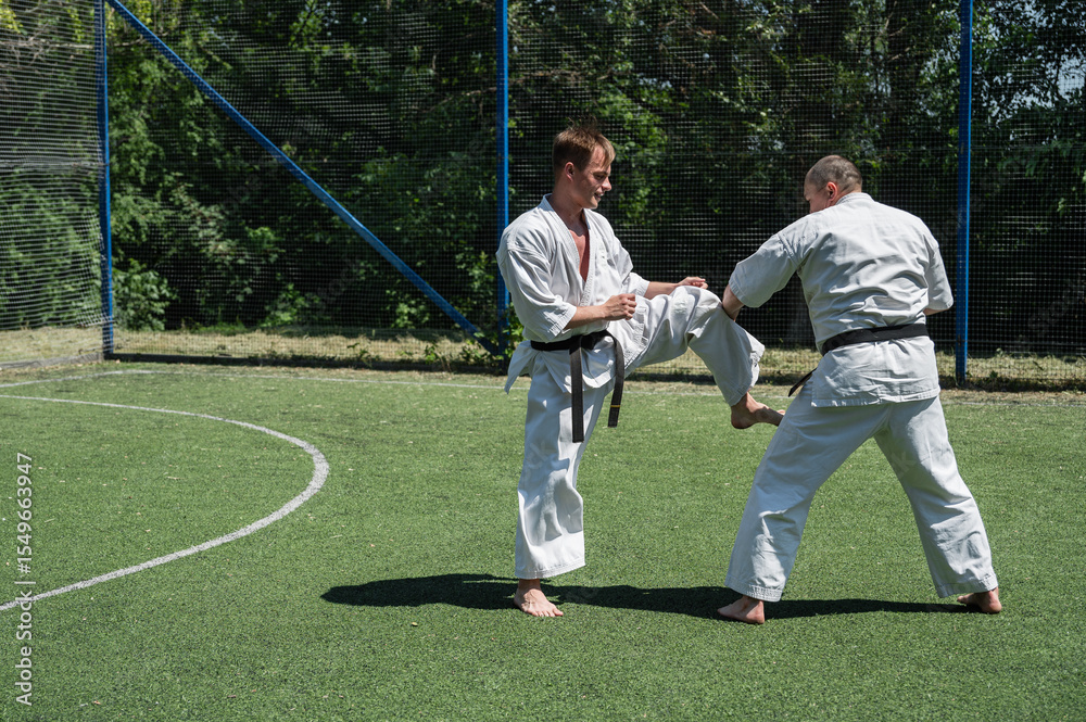 Obraz premium Man in white karate gi delivering a front kick to his sparring partner.