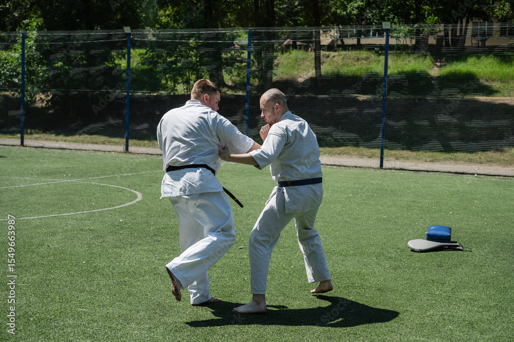 Obraz premium Karate fighters practicing blocking and striking techniques outside.