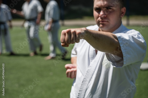 Karate student practicing punch with group outdoors.