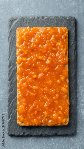 Delicious gourmet cracker topped with vibrant orange fruit spread on a slate serving board