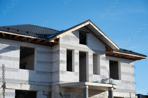 Building under construction with aerated concrete blocks and roof tiles against blue sky, representing housing development and real estate investment