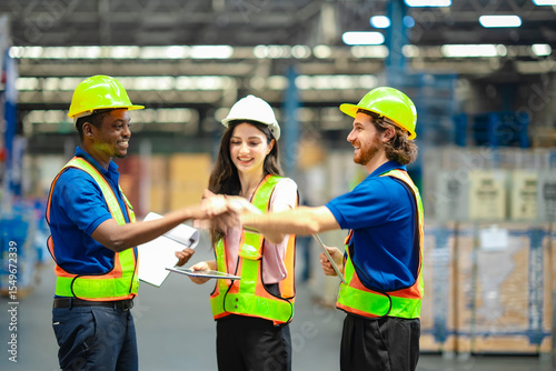 Happy warehouse workers in safety vests and helmets celebrating success with raised hands. Team achievement, productivity, and positive collaboration in industrial logistics environment.
