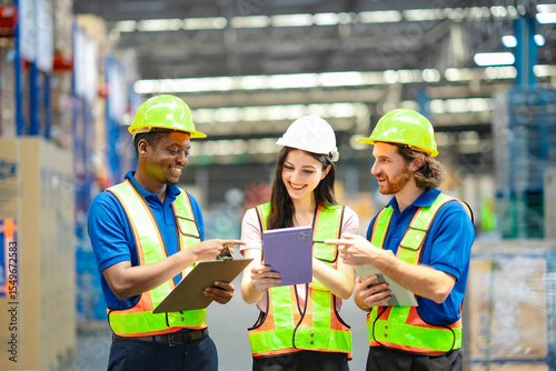 Industrial warehouse team using digital devices to plan inventory flow. Smart logistics solutions, teamwork, PPE, and warehouse coordination in modern supply chain system.