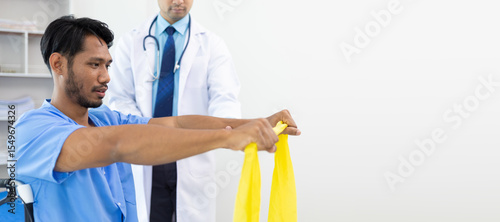 Physiotherapist doctor in hospital is practicing physical therapy on a male patient to rehabilitate arm muscles with elastic bands.