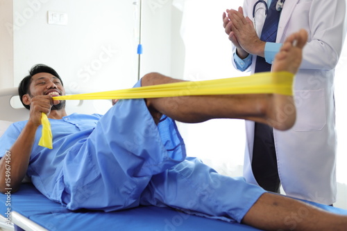 Physiotherapist doctor in hospital is practicing physical therapy on a male patient to rehabilitate leg muscles with elastic bands.