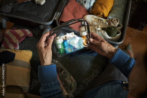 Photos Hands of senior carefully packing medications and toiletries into clear bags for