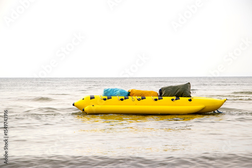 A bright yellow inflatable banana bobs on sea waves, shining under the summer sun. This fun water attraction awaits new riders for a seaside adventure.