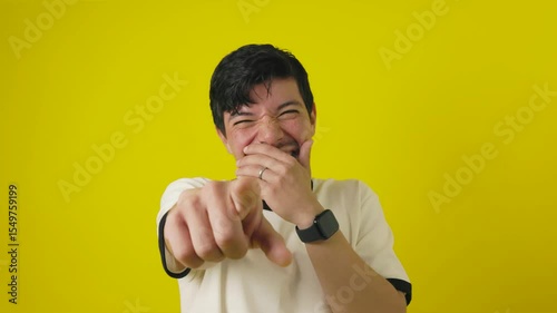 Young freckled man with a cheerful mustache mockingly pointing with his hand on a yellow background with copyspace, concept of young man pointing in mockery