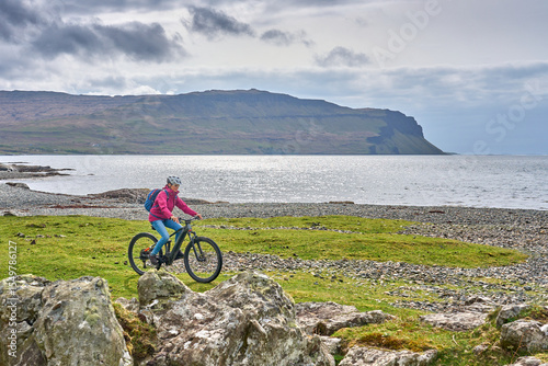 active senior woman riding her electric mountain bike between blooming gorse in the wetlands of the Isle of Mull in Scotland, UK
