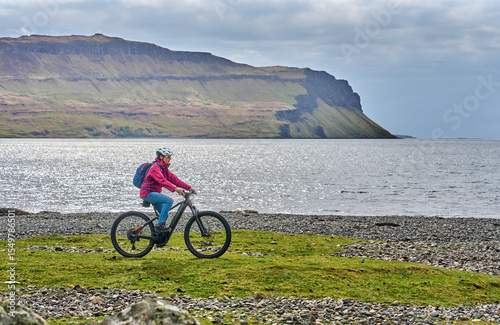 active senior woman riding her electric mountain bike between blooming gorse in the wetlands of the Isle of Mull in Scotland, UK