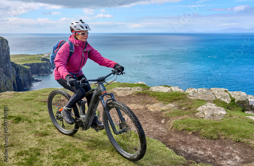 active senior woman riding her electric mountain bike on the cliffs of nest point lighthouse on the Isle of Skye in Scotland, UK
