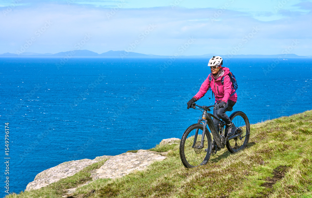 Fototapeta premium active senior woman riding her electric mountain bike on the cliffs of nest point on the Isle of Skye in Scotland, UK