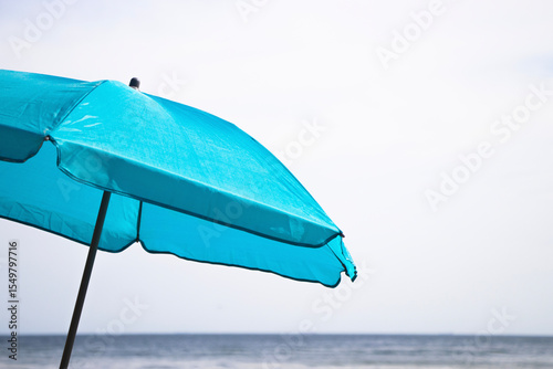 A blue beach umbrella stands on the sandy shore by the sea, offering shade under the warm sun on a peaceful summer day.