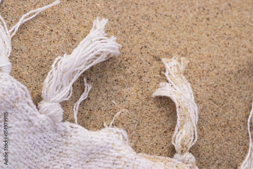Close-up of white woven towel fringe on golden sand. Natural beach background with soft texture and summery coastal vibe. Perfect for travel and relaxation themes
