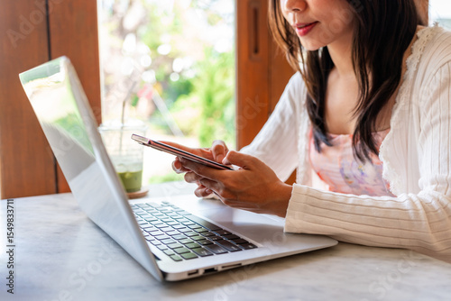 Young Asian woman with drinks using phone and working with laptop in cafe, Modern lifestyle