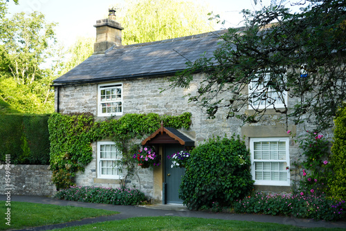 Ashford in the Water, Derbyshire, England - June 20 2025: A charming stone cottage with lush green ivy, flower baskets, and a tranquil atmosphere.