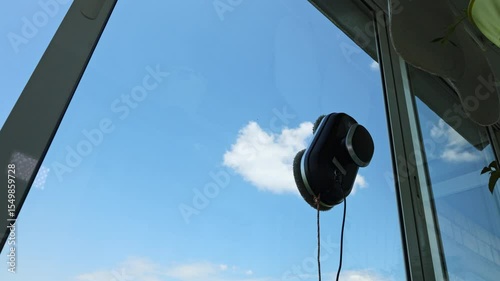 Robot window cleaner works washing a window against a beautiful blue sky with lush clouds on a bright sunny day