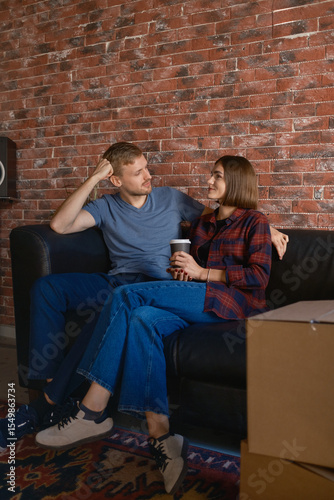 Young couple sitting on sofa together, drinking coffee, and enjoying a comfortable moment.