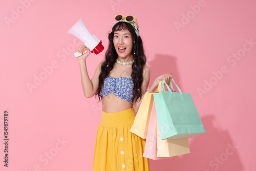 Excited Asian woman in summer outfit holding megaphone and shopping bags. Perfect for sales announcements, promotions, or summer offers.