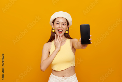 Happy beautiful young Asian woman showing smartphone mockup blank screen isolated on yellow background.