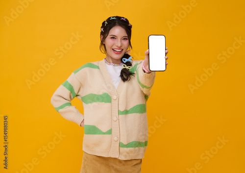 Happy beautiful young Asian woman showing smartphone mockup blank screen isolated on yellow background.
